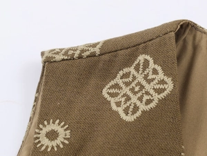 Détail de la broderie ethnique beige sur le tissu en lin marron de l'épaule du gilet