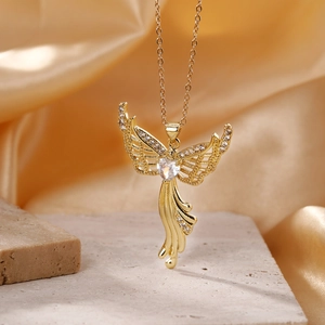 Golden angel wing necklace with a heart-shaped zircon pendant on a luxury silk background