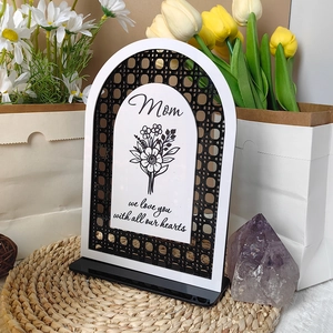 Detail of white acrylic Mom heart sign with black floral pattern on a woven mat
