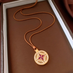 Detailed close-up of a vintage hollow floral pendant with red marquise stones and silk cord