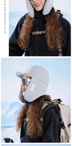Close-up of light gray winter trapper hat with ear flaps on snowy mountain background