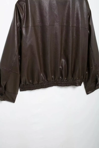 Detail of faux leather bomber jacket featuring elastic waist hem and buttoned cuffs