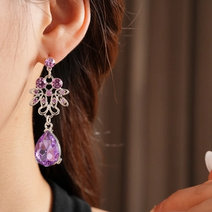 Close-up of purple teardrop crystal earring with intricate silver floral metalwork detail