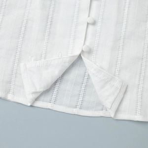 Detail of white blouse featuring fabric covered buttons and vertical textured stripes