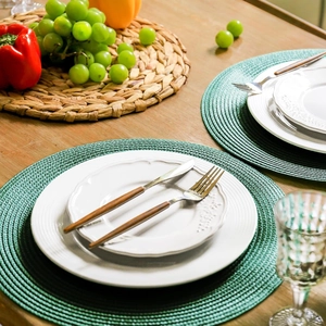 Macro shot of green round woven place mats with white plates and wooden cutlery