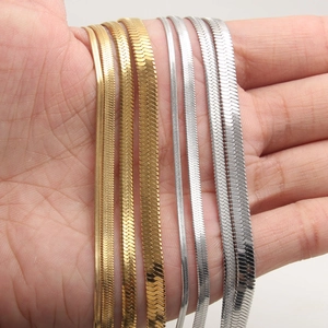 Flat herringbone snake chains in gold and silver steel, varying widths held in hand
