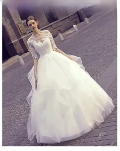 Detail of elegant lace floral neckline and sheer sleeves on white tiered bridal gown