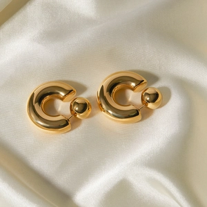 Detail of C-shaped gold polished earrings with sphere accent on cream silk background
