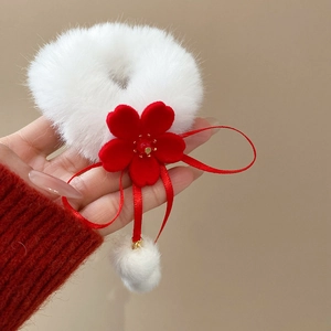 Close-up of plush white hair scrunchie with red velvet flower and hanging fur ball tassels