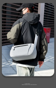 Back view of model wearing light gray waterproof crossbody bag in modern outdoor setting