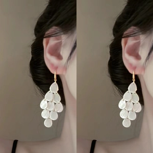 Detail view of long white teardrop sequin earrings with gold hooks on a model