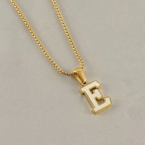 Detail of golden box chain with white enamel letter E pendant on gray fabric