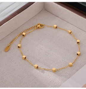 Détail d'une chaîne de cheville minimaliste en titane doré avec des perles cubiques