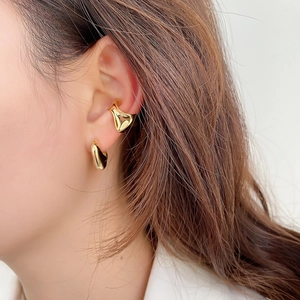 Dettaglio del set di ear cuff e orecchino dorato irregolare indossato da una modella