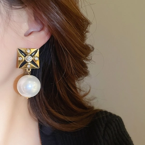 Close-up of vintage square stud earring with black enamel and white pearl drop on model