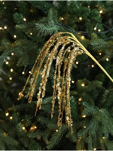 Close-up of golden sequin Christmas branch with glitter tassel against blurry holiday lights