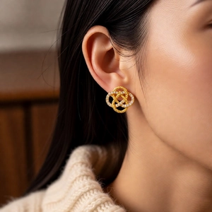 Close-up of elegant gold woven knot stud earrings with zircons worn by a model
