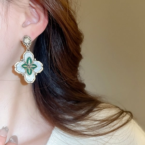 Gros plan de boucles d'oreilles fleurs vintage en émail vert et blanc sur un mannequin