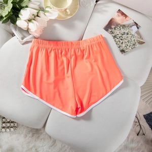Bright orange sports shorts with elastic waistband and white piping on gray surface