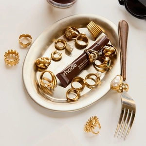 Elegant gold pearl rings and jewelry set displayed with lip tint on a metal tray