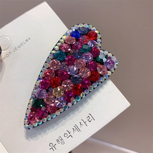 Macro shot of heart-shaped hair clip with colorful crystals on white packaging card