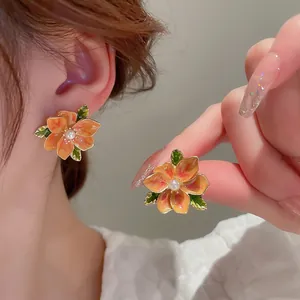 Elegant floral stud earrings with orange petals and center pearl on a female model