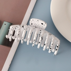 Detail shot of a white large hair claw clip with black ink splatter pattern on a dish