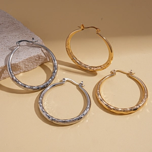 Geometric textured gold and silver hoop earrings on a stone background