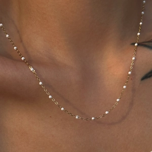 Close-up of 18k gold plated stainless steel choker with white enamel beads on a model