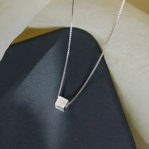 Macro detail of silver cube pendant with brushed matte texture on a box chain