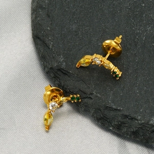 Golden banana-shaped stud earrings with yellow and green crystals on stone background
