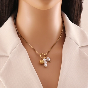 Collana dorata elegante con perle e quadrifoglio su modella con abito dai colori chiari
