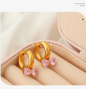 Macro detail of gold hoop earrings with pink bow-shaped zircon pendants on beige velvet
