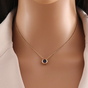 Detail of a gold stainless steel necklace with a round blue gemstone on a female neck