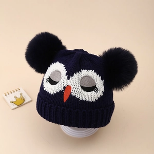 Détail du bonnet en tricot bleu foncé avec broderie hibou et deux pompons en fourrure douce