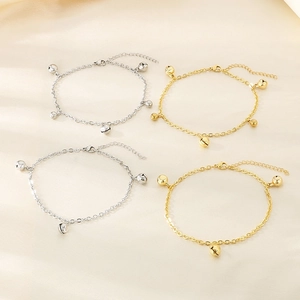 Détail de bracelets de cheville à clochettes or et argent sur un fond en soie douce