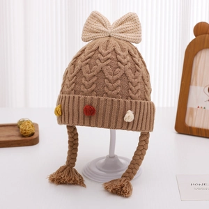 Dettaglio di un cappello in maglia marrone per neonati con fiocco e trecce