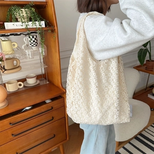 Detail view of a white floral lace tote bag with daisy embroidery on a model shoulder