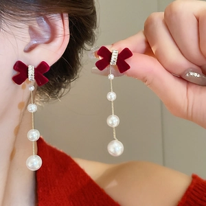 Macro shot of burgundy velvet bow earrings with dangling white pearls and metal chains
