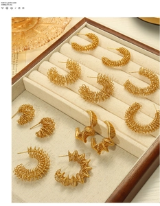 Détails de boucles d'oreilles créoles dorées en spirale sur un plateau beige