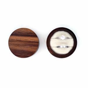 Top-down view of round dark wood ring box with white velvet lining and silver rings