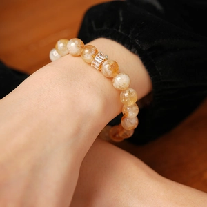 Détail macro d'un bracelet en perles ambrées avec un charm doré en zircon au poignet