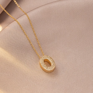 Macro detail of gold letter O pendant with cubic zirconia on champagne silk fabric