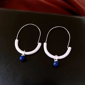 Macro view of silver U-shaped hoop earrings featuring a textured finish and blue lapis bead