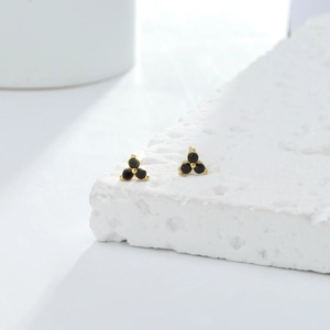 Detailed macro view of triangular gold stud earrings featuring three black zircon stones