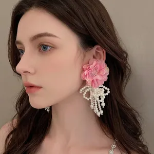 Exaggerated pink silk flower earrings with cascading pearl tassels worn on a model