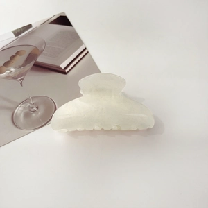 Close-up of a white translucent hair claw clip with subtle glitter on a minimalist table