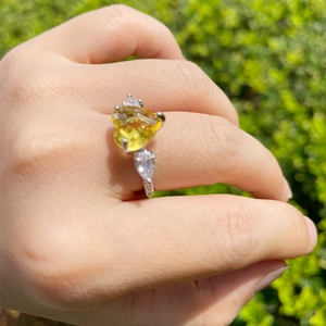 Close-up of heart-shaped yellow gemstone ring with pear-cut side stones on hand