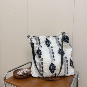 Close-up of ethnic blue embroidery on a white linen tote bag with black leather straps
