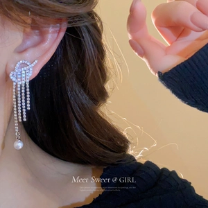 Close-up of silver tassel earrings with sparkling rhinestones and a hanging pearl on ear